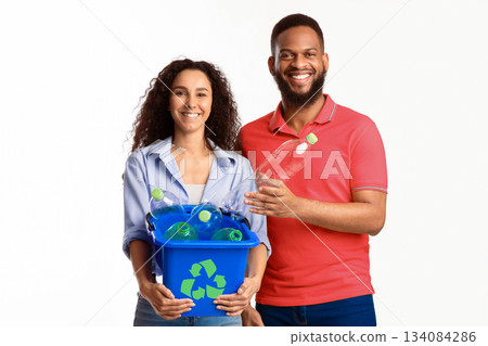 Diverse Family Couple Holding Box With Recycle Symbol Putting Used Plastic Bottle To Garbage Container Posing Standing Over White Background, Smiling To Camera. Waste Sorting, Junk Disposal 134084286