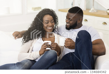 Enjoying Weekend. Young African Couple In Love Spending Time Together, Cuddling And Drinking Coffee on Couch at Home, Copy Space Enjoying Weekend. Young African Couple In Love Spending Time Together, Cuddling And Drinking Coffee on Couch at Home, Copy Space 134084342