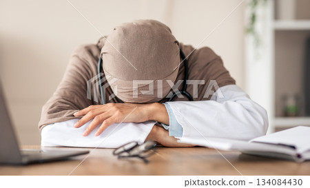 Overworked female doctor woman in hijab having nap at workdesk, working with laptop in clinic. Exhausted physician young lady leaning on her hands, needs for break during long working day Overworked female doctor woman in hijab having nap at workdesk, working with laptop in clinic. Exhausted physician young lady leaning on her hands, needs for break during long working day 134084430