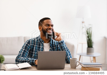 Smiling Black Businessman Talking On Phone Sitting At Workplace In Modern Office. Mobile Business Communication And Entrepreneurship. Man Having Cellphone Conversation At Work. 134084495