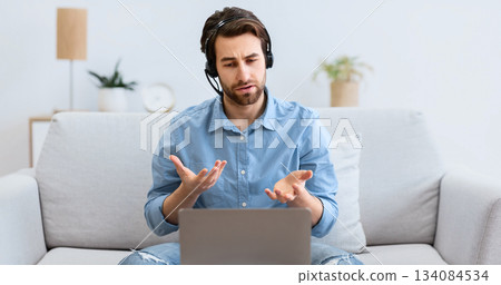 Guy In Headphones At Laptop Talking To Computer Screen Making Video Call Working Remotely Sitting On Sofa At Home. Distant Communication, Online Business Course Training Concept Guy In Headphones At Laptop Talking To Computer Screen Making Video Call Working Remotely Sitting On Sofa At Home. Distant Communication, Online Business Course Training Concept 134084534