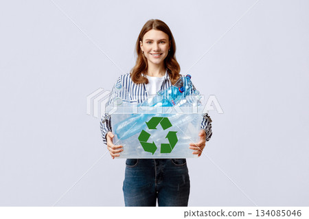 Waste Reuse. Cheerful Young Woman Carrying Container With Plastic Bottles For Recycling And Smiling At Camera, Happy Eco-Activist Sorting Garbage For Recycle, Standing On Grey Background 134085046