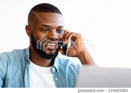 Closeup Shot Of Cheerful African American Guy Talking On Cellphone And Working On Laptop At Home Office, Smiling Black Freelancer Man Looking At Computer Screen, Enjoying Remote Work, Copy Space Closeup Shot Of Cheerful African American Guy Talking On Cellphone And Working On Laptop At Home Office, Smiling Black Freelancer Man Looking At Computer Screen, Enjoying Remote Work, Copy Space 134085065