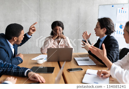 Discontented Coworkers Shouting At Unhappy Victimized Businesswoman Sitting At Table In Modern Office. Adult Bullying At Work, Conflicts And Disagreement, Business Communication Problems Concept 134085241