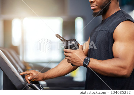Unrecognizable black guy sportsman with protein drink standing on treadmill, side view, copy space. Cropped of muscular african american man having jogging work out, drinking water, sun flare Unrecognizable black guy sportsman with protein drink standing on treadmill, side view, copy space. Cropped of muscular african american man having jogging work out, drinking water, sun flare 134085252