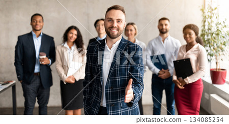 Smiling Businessman HR Stretching Hand For Handshake Greeting To Camera Standing With Business Team In Modern Office. Recruitment And Employment, Career Offer Concept. Selective Focus, Panorama Smiling Businessman HR Stretching Hand For Handshake Greeting To Camera Standing With Business Team In Modern Office. Recruitment And Employment, Career Offer Concept. Selective Focus, Panorama 134085254