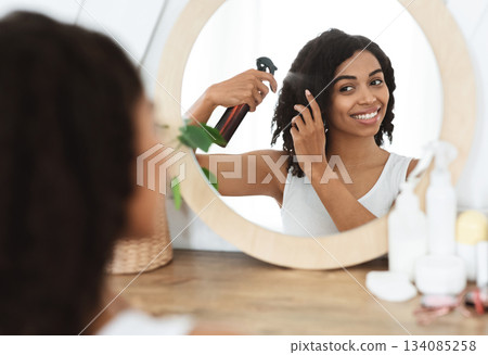 Hairstyling. Beautiful Black Woman Using Hair Spray For Easy Combing, Standing Near Mirror At Home, Selective Focus Hairstyling. Beautiful Black Woman Using Hair Spray For Easy Combing, Standing Near Mirror At Home, Selective Focus 134085258