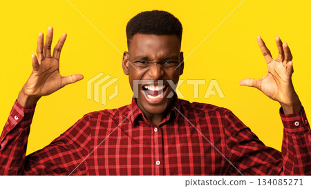 Portrait of young angry black man shouting with rage, furious african american guy raising hands and screaming with anger while standing isolated over yellow background, closeup with copy space Portrait of young angry black man shouting with rage, furious african american guy raising hands and screaming with anger while standing isolated over yellow background, closeup with copy space 134085271