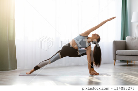 Well fit young lady in sportswear having yoga practice at home, standing in triangle pose, copy space. Active woman stretching her body in living room, exercising while staying on self-isolation Well fit young lady in sportswear having yoga practice at home, standing in triangle pose, copy space. Active woman stretching her body in living room, exercising while staying on self-isolation 134085275