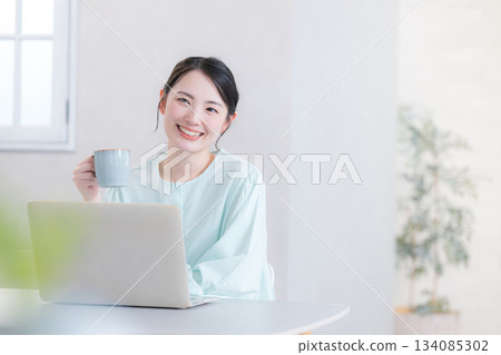 Woman drinking coffee while using a computer, looking up 134085302