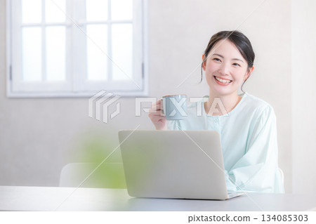 Woman drinking coffee while using a computer, looking up 134085303