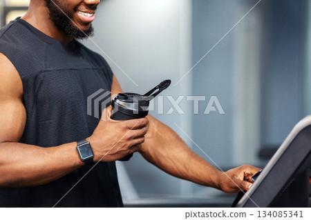 Cropped of muscular african american man having jogging work out, pressing on button. Unrecognizable black guy sportsman with protein drink standing on treadmill, side view, copy space, closeup Cropped of muscular african american man having jogging work out, pressing on button. Unrecognizable black guy sportsman with protein drink standing on treadmill, side view, copy space, closeup 134085341