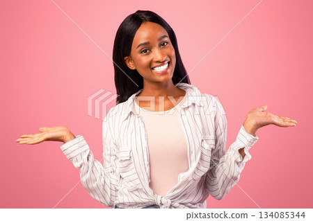 Young black woman comparing options, making scales with her hands, holding invisible objects on pink studio background, mockup. African American lady advertising your products Young black woman comparing options, making scales with her hands, holding invisible objects on pink studio background, mockup. African American lady advertising your products 134085344