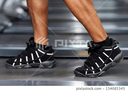 Sports shoes for gym concept. Closeup of unrecognizable african american man bodybuilder legs walking by treadmill, wearing black and white sneakers, selective focus on shoes, gym interior, copy space Sports shoes for gym concept. Closeup of unrecognizable african american man bodybuilder legs walking by treadmill, wearing black and white sneakers, selective focus on shoes, gym interior, copy space 134085345