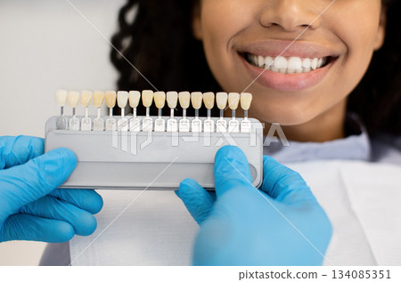 Stomatologist Doctor In Blue Gloves Holding Dental Teeth Shade Guide Chart, Choosing Right Emanel Color For Female Patient During Medical Treatment In Modern Stomatological Clinic, Cropped, Closeup 134085351