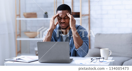 African American Businessman Having Headache Sitting At Laptop Computer Working From Home. Black Man Massaging Temples Suffering From Migraine Pain Indoor. Selective Focus 134085473