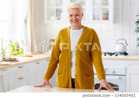 Happy attractive senior lady posing in cozy white kitchen at home, copy space. Cheerful old woman with grey short hair smiling at camera, chilling after cooking dinner for her family Happy attractive senior lady posing in cozy white kitchen at home, copy space. Cheerful old woman with grey short hair smiling at camera, chilling after cooking dinner for her family 134085481