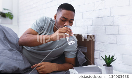 Black Man Taking Glass Of Water Lying In Bed, Hydrating Drinking In Bedroom At Home In The Morning, Starting New Day With Fresh Aqua. Stay Hydrated. Healthy Liquid Concept. Selective Focus Black Man Taking Glass Of Water Lying In Bed, Hydrating Drinking In Bedroom At Home In The Morning, Starting New Day With Fresh Aqua. Stay Hydrated. Healthy Liquid Concept. Selective Focus 134085488
