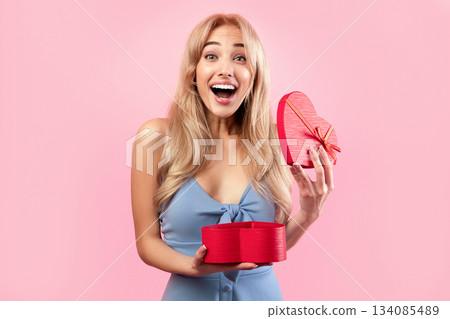 Excited blonde woman opening heart shaped gift box for Valentine's Day over pink studio background. Gorgeous millennial lady happy to receive present for lover's holiday Excited blonde woman opening heart shaped gift box for Valentine's Day over pink studio background. Gorgeous millennial lady happy to receive present for lover's holiday 134085489