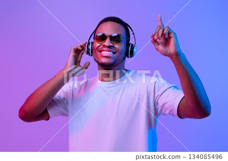 Happy African American Guy In Neon Light Listening Music In Wireless Headphones And Dancing, Cheerful Young Black Man Having Fun Over Purple Background, Enjoying His Favorite Songs, Copy Space Happy African American Guy In Neon Light Listening Music In Wireless Headphones And Dancing, Cheerful Young Black Man Having Fun Over Purple Background, Enjoying His Favorite Songs, Copy Space 134085496