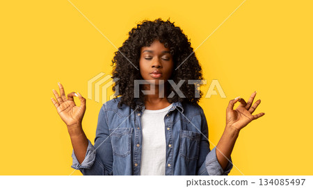 Staying calm and relaxed in urban atmosphere. Cute determined dark-skinned woman in casual outfit, closing eyes and raising hands in zen gesture, meditating or practicing yoga over yellow background Staying calm and relaxed in urban atmosphere. Cute determined dark-skinned woman in casual outfit, closing eyes and raising hands in zen gesture, meditating or practicing yoga over yellow background 134085497