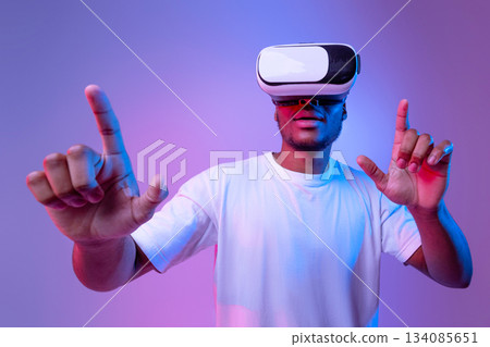 Gaming Technologies. Excited African American Guy In VR Glasses Playing Video Game, Experiencing Virtual Reality While Standing Under Neon Lighting Over Purple Background, Closeup Shot, Free Space Gaming Technologies. Excited African American Guy In VR Glasses Playing Video Game, Experiencing Virtual Reality While Standing Under Neon Lighting Over Purple Background, Closeup Shot, Free Space 134085651