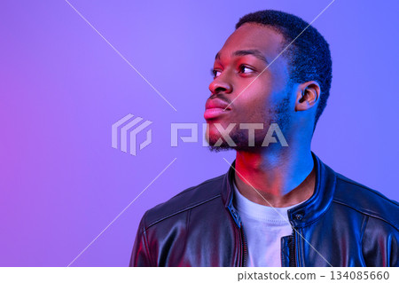 Handsome Young African American Man In Stylish Leather Jacket Looking Aside, Attractive Millennial Black Guy Standing Under Neon Lighting Over Purple Background, Closeup Shot With Free Space Handsome Young African American Man In Stylish Leather Jacket Looking Aside, Attractive Millennial Black Guy Standing Under Neon Lighting Over Purple Background, Closeup Shot With Free Space 134085660