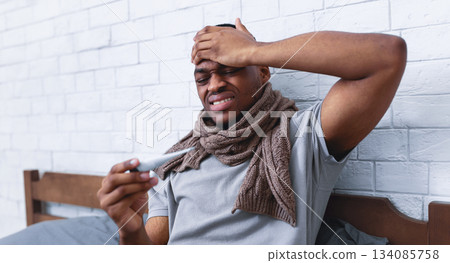 Fever And Flu. Ill Black Guy Touching Forehead Holding Thermometer Having Influenza Symptoms And Headache Sitting In Bed Indoors. Covid-19 Virus, Seasonal Health Problems. Selective Focus Fever And Flu. Ill Black Guy Touching Forehead Holding Thermometer Having Influenza Symptoms And Headache Sitting In Bed Indoors. Covid-19 Virus, Seasonal Health Problems. Selective Focus 134085758