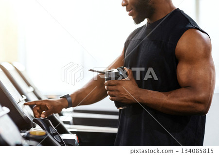 Cropped of muscular african american man holding sports drink, standing on treadmill, drinking protein before running, panorama with copy space. Unrecognizable black bodybuilder jogging at gym Cropped of muscular african american man holding sports drink, standing on treadmill, drinking protein before running, panorama with copy space. Unrecognizable black bodybuilder jogging at gym 134085815