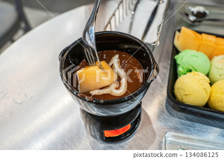 Dipping melon in chocolate fondue Dipping melon in chocolate fondue 134086125