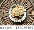 Tempe Mendoan, an Indonesian traditional snack made from tempe or tempeh (fermented soybeans) coated in flour and spring onions and fried half-cooked, on a white enamel plate, placed on a rattan table 134086165