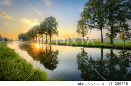 The Beautiful Serene Sunset Over a Tranquil and Calm River Surrounded by Lush Greenery The Beautiful Serene Sunset Over a Tranquil and Calm River Surrounded by Lush Greenery 134086856