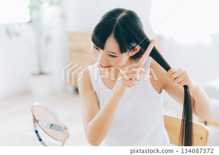 A young woman using a hair iron 134087372