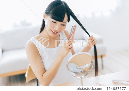 A young woman using a hair iron 134087377