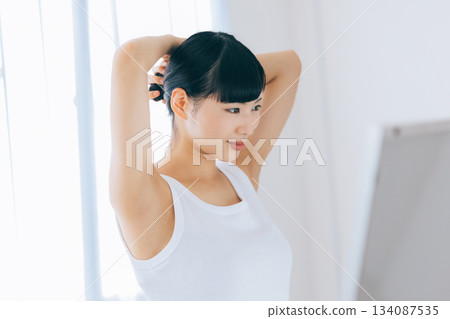 A young woman tying her hair while holding a toothbrush in her mouth A young woman tying her hair while holding a toothbrush in her mouth 134087535