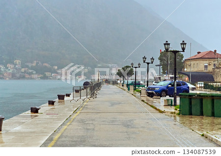Wet Embankment in a Coastal Town on a Foggy Overcast Day with a View of Mountains and Old Houses 134087539
