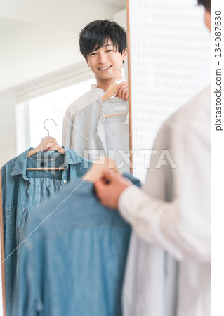 A young Asian man coordinating his clothes while looking in the mirror A young Asian man coordinating his clothes while looking in the mirror 134087630