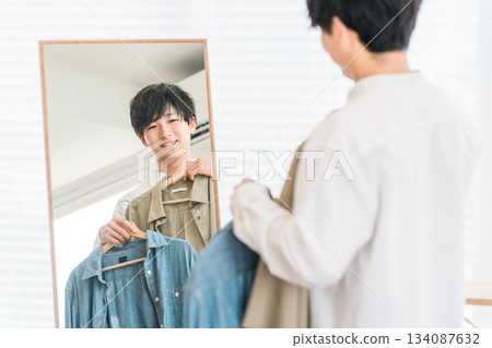 一位年輕的亞裔男子正在照鏡子搭配衣服。 一位年輕的亞裔男子正在照鏡子搭配衣服。 134087632