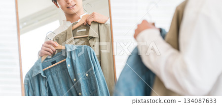 一位年輕的亞裔男子正在照鏡子搭配衣服。 134087633