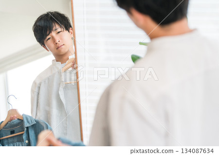 一位年輕的亞裔男子正在照鏡子搭配衣服。 134087634