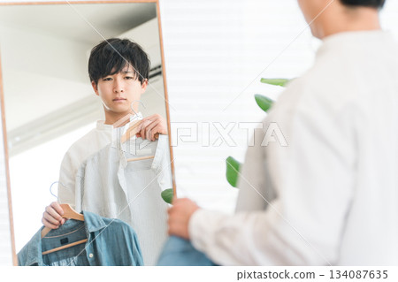 A young Asian man coordinating his clothes while looking in the mirror 134087635