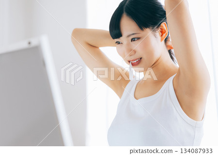A young woman tying her hair while holding a toothbrush in her mouth A young woman tying her hair while holding a toothbrush in her mouth 134087933