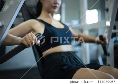 Young woman training chest on a weight machine in a gym Young woman training chest on a weight machine in a gym 134089067