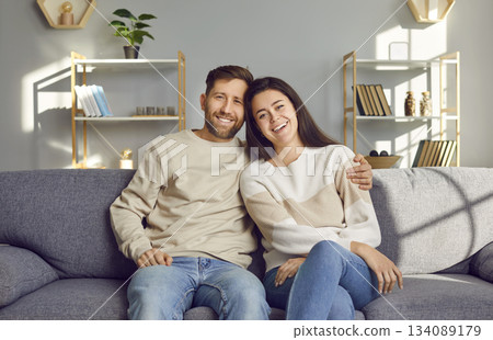 Portrait of a cheerful, smiling young married couple sitting on the sofa at home Portrait of a cheerful, smiling young married couple sitting on the sofa at home 134089179