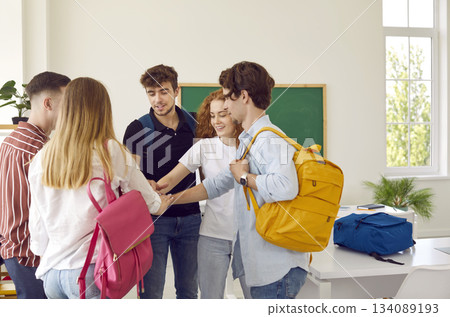 Group of students standing close in circle joining their hands in classroom 134089193