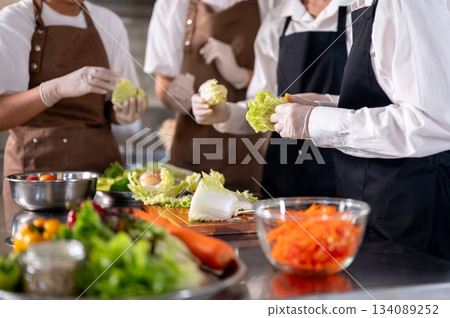 Close up of chef and her assistants separating cabbage leaves while standing around kitchen counter. Close up of chef and her assistants separating cabbage leaves while standing around kitchen counter. 134089252
