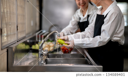 Asian female chefs is washing or cleaning a green pepper with tab water in restaurant's kitchen sink Asian female chefs is washing or cleaning a green pepper with tab water in restaurant's kitchen sink 134089401