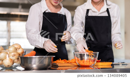 Close up of a hand in rubber gloves touching sliced carrots in the glass bow on kitchen counter. 134089405