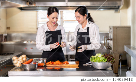 Female chef teaching how to cut a tomato to her student or an assistant at kitchen cooking counter. 134089418