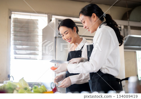 A student or assistant showing how she cut carrots to a female chef at kitchen cooking counter. A student or assistant showing how she cut carrots to a female chef at kitchen cooking counter. 134089419